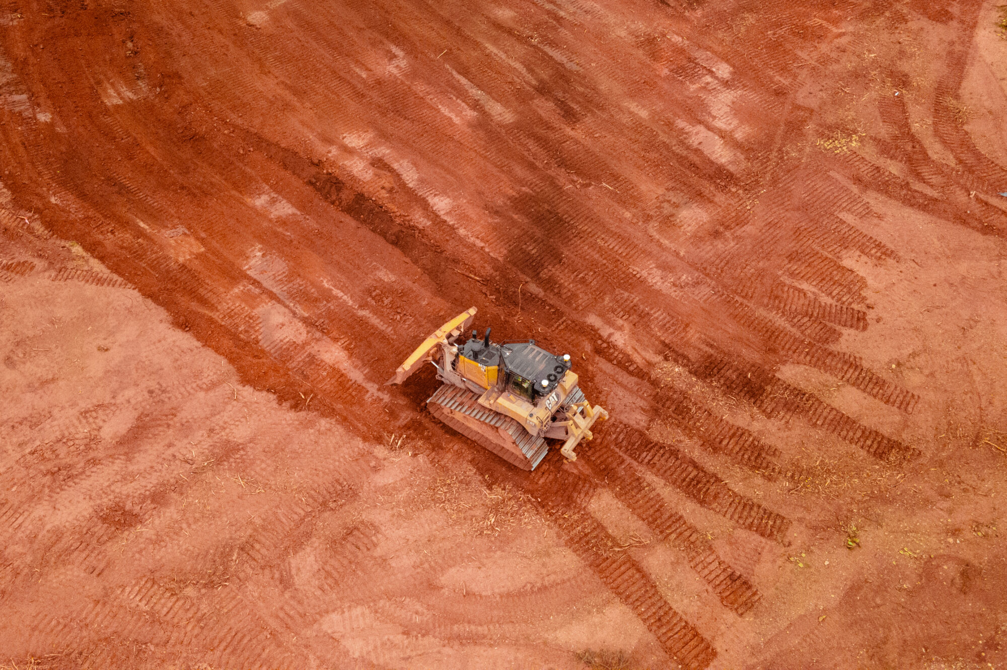 Bulldozer grading red dirt, tracks visible, sparse edge vegetation.