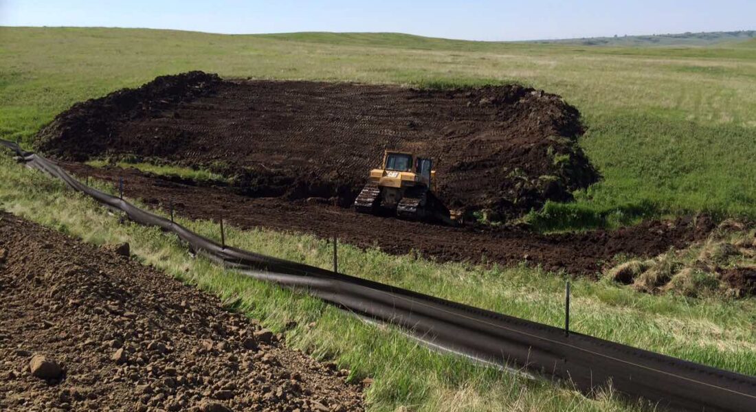 Bulldozer leveling soil near grassy fields and black silt fence.