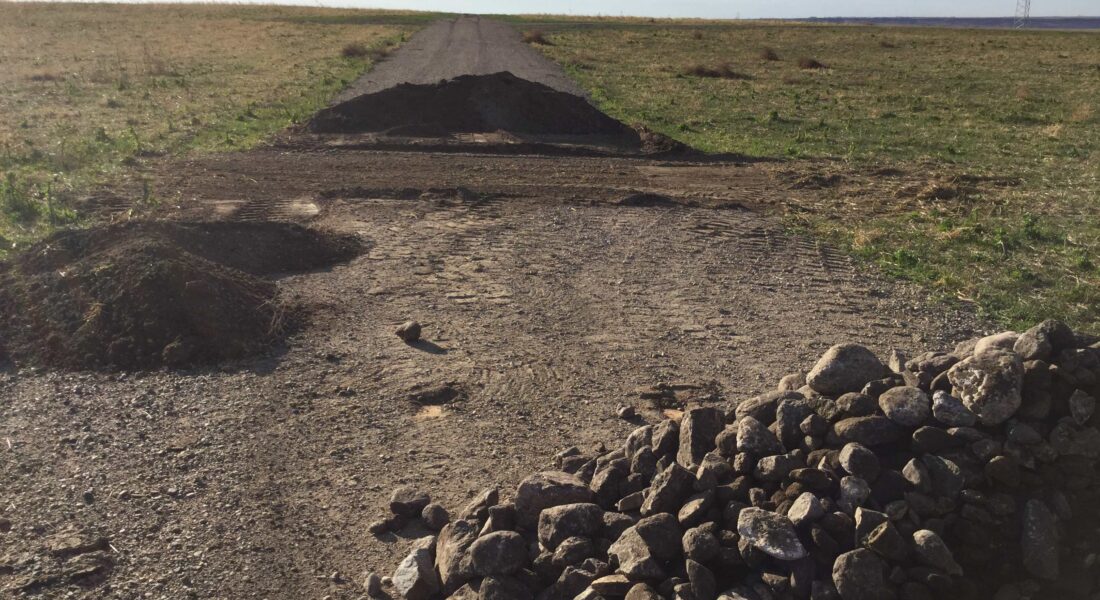 Gravel road under construction with rocks and unfinished section ahead.
