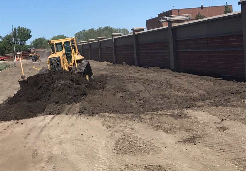 Yellow bulldozer moves dirt next to tall concrete wall.