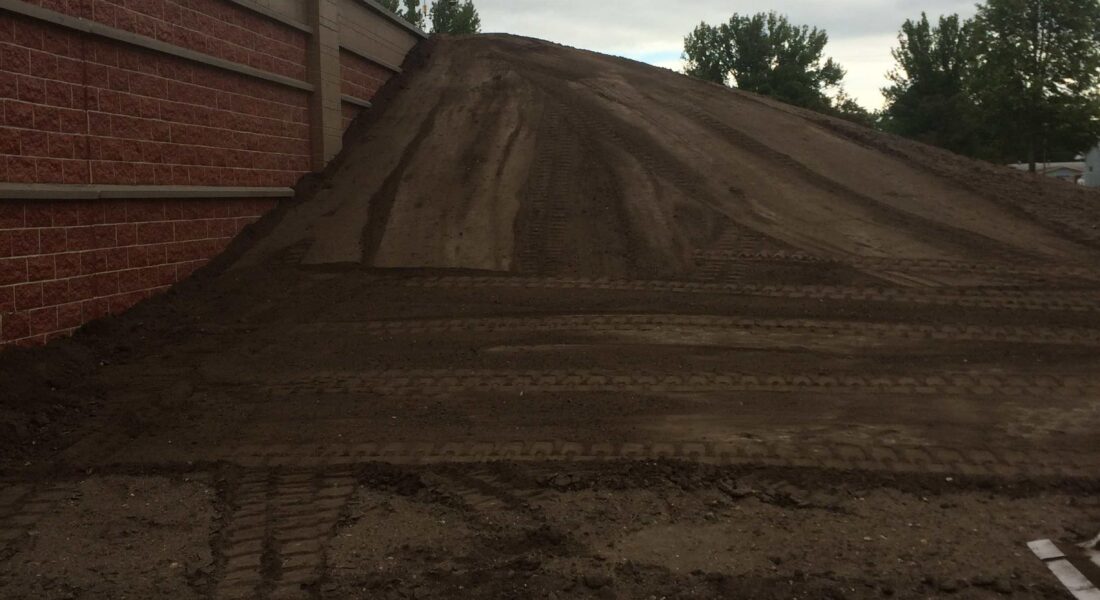 Dirt mound by red brick wall, tire tracks visible, cloudy sky.