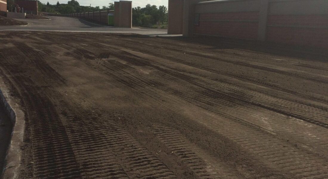 Dirt lot with tire tracks, brick wall, and curved curb.