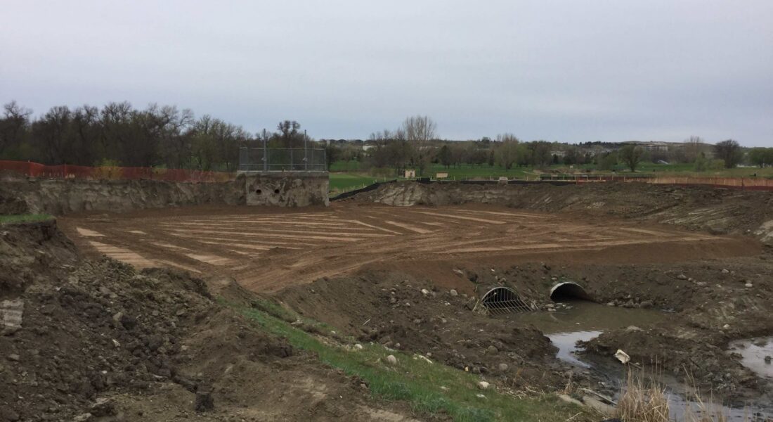 Leveled dirt area with pipes, fencing, and surrounding soil mounds.