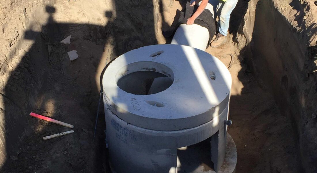 Worker in safety vest installs concrete drainage structure in trench.