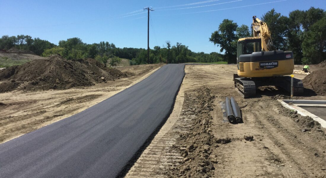 New paved path, construction equipment, dirt piles, excavator, pipes.