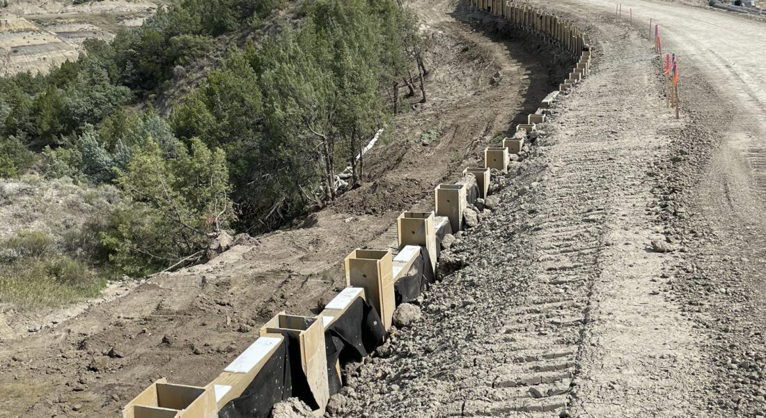 Curving dirt road by hillside with barriers and equipment.