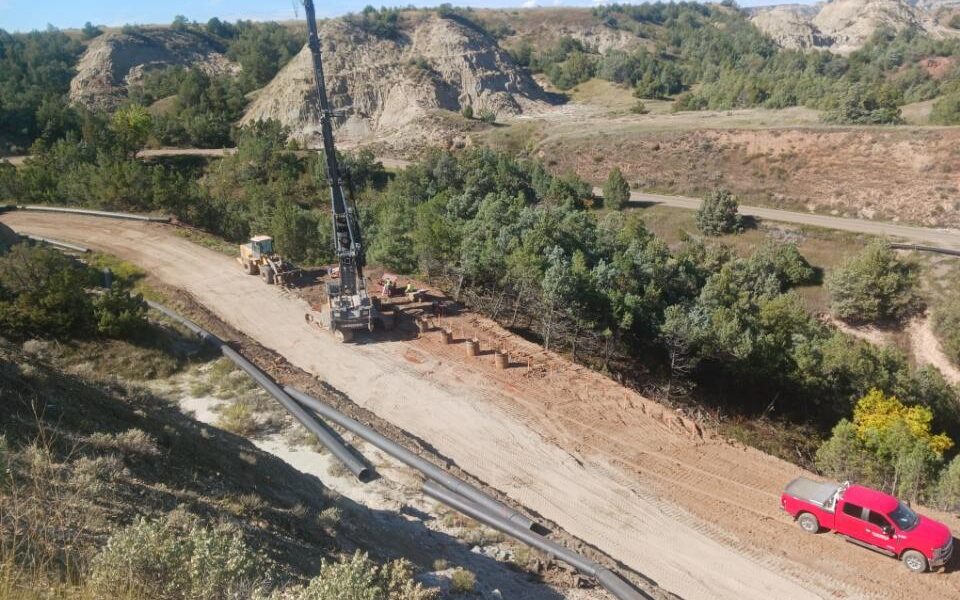 Construction site with crane, red truck, equipment, pipes on dirt road.