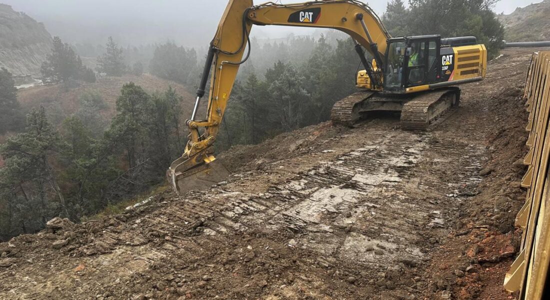 Yellow Caterpillar excavator levels dirt on foggy hillside.