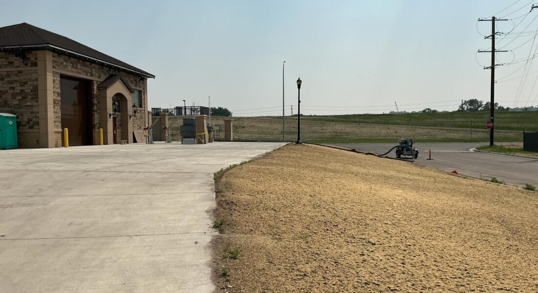 Curved concrete path by brick building; dirt and open sky.