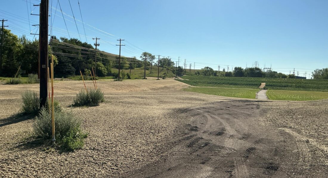 Outlook of grass and walk path with dirt in the foreground, utility poles on left, clear sky, text overlay.