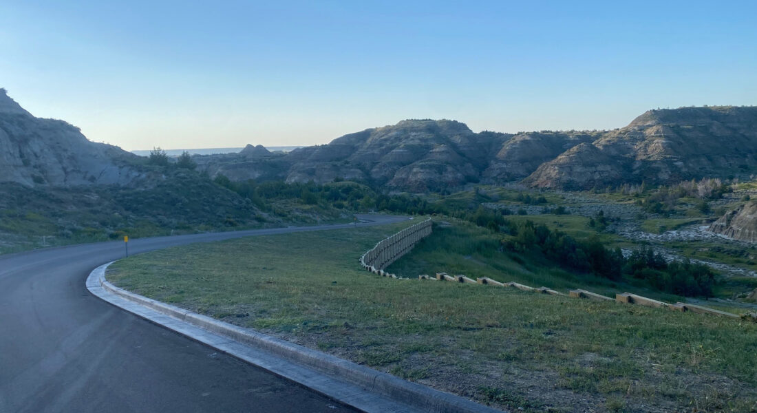 Curved paved road in grassy valley, rocky hills, overlay text.