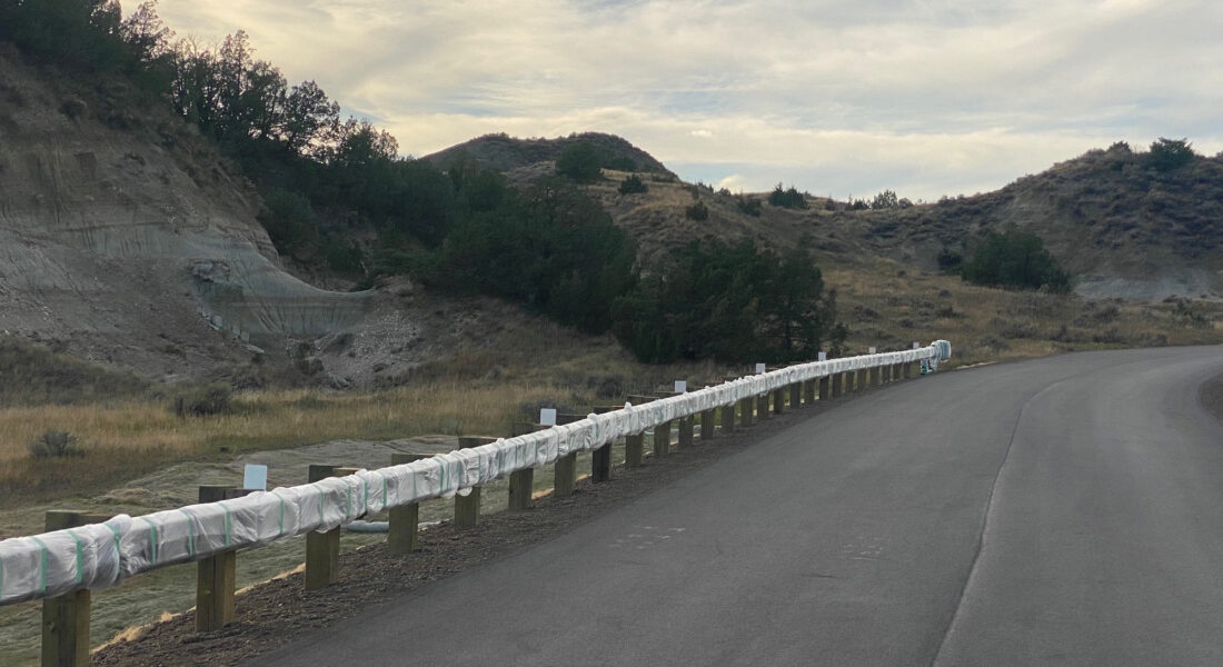 Curved paved road in hilly terrain, guardrail left; overcast sky.
