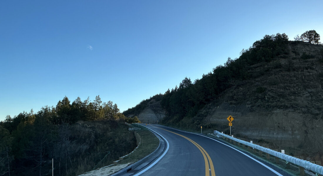 Curved road with yellow lines in hilly forest, clear sky.