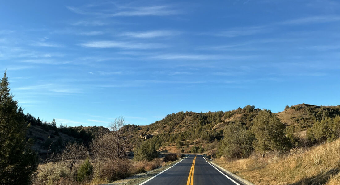 Rural two-lane road with hills, trees, sky, and yellow text overlay.