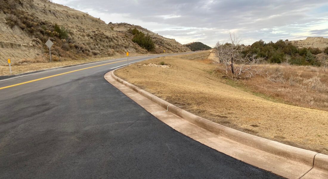 Curving paved road in grassy hills, cloudy sky, yellow text overlays.
