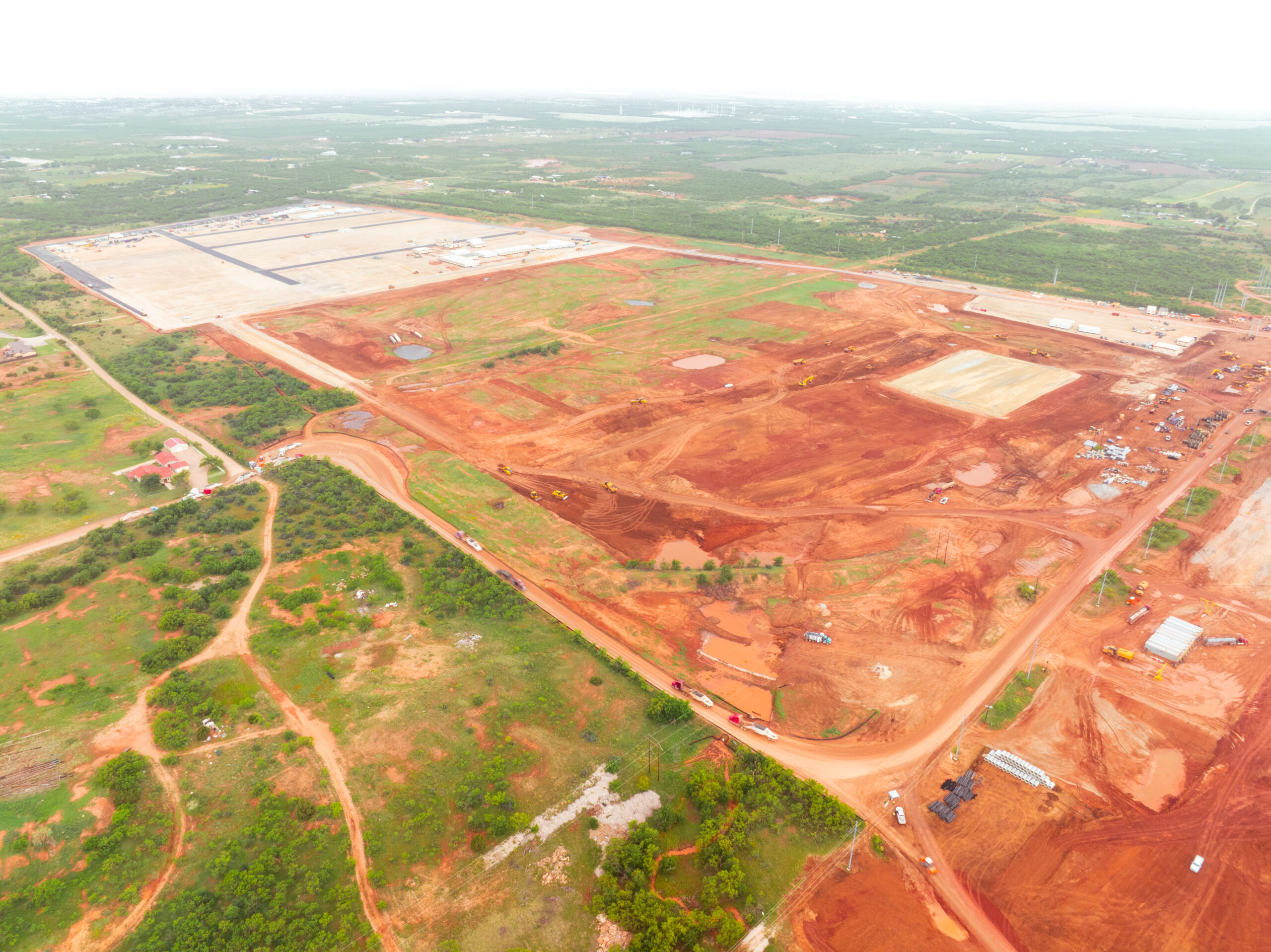 Aerial view of construction site with red earth and vehicles.