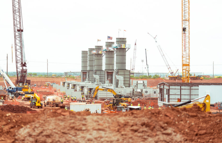 Cranes, machinery, and workers by towers with flags above.