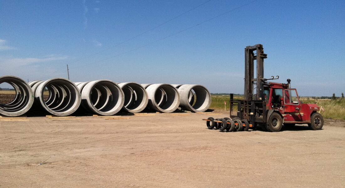Red forklift by concrete pipes on a dirt lot.