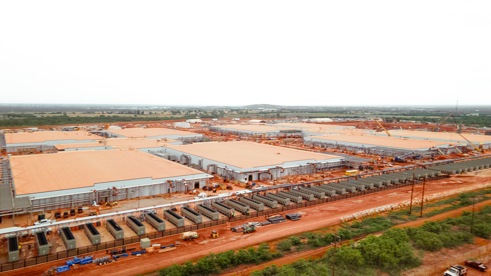 Industrial site with wide buildings, vehicles, and red earth.