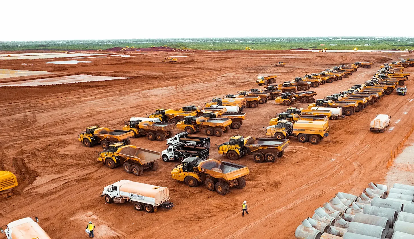 Aerial view of lined-up construction vehicles on red dirt site.