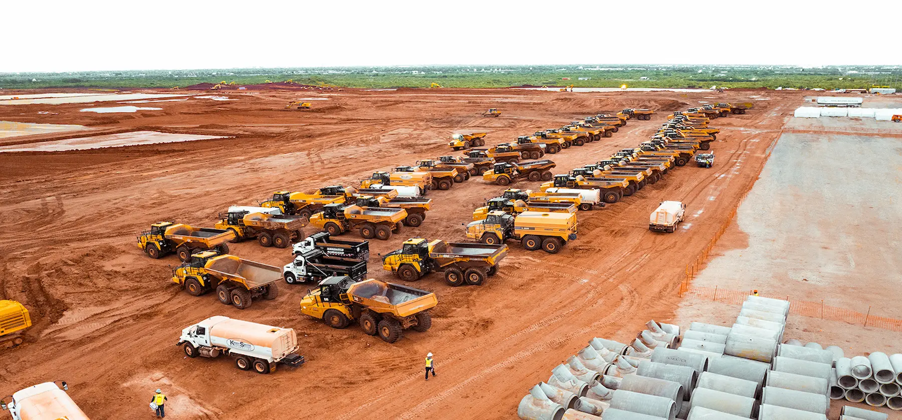 Aerial view of lined-up construction vehicles on red dirt site.