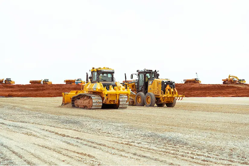 Construction site with yellow bulldozers and loaders on dirt.