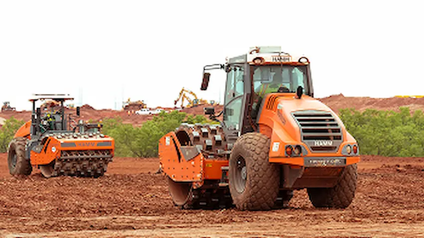 Two orange road rollers work on soil at construction site.