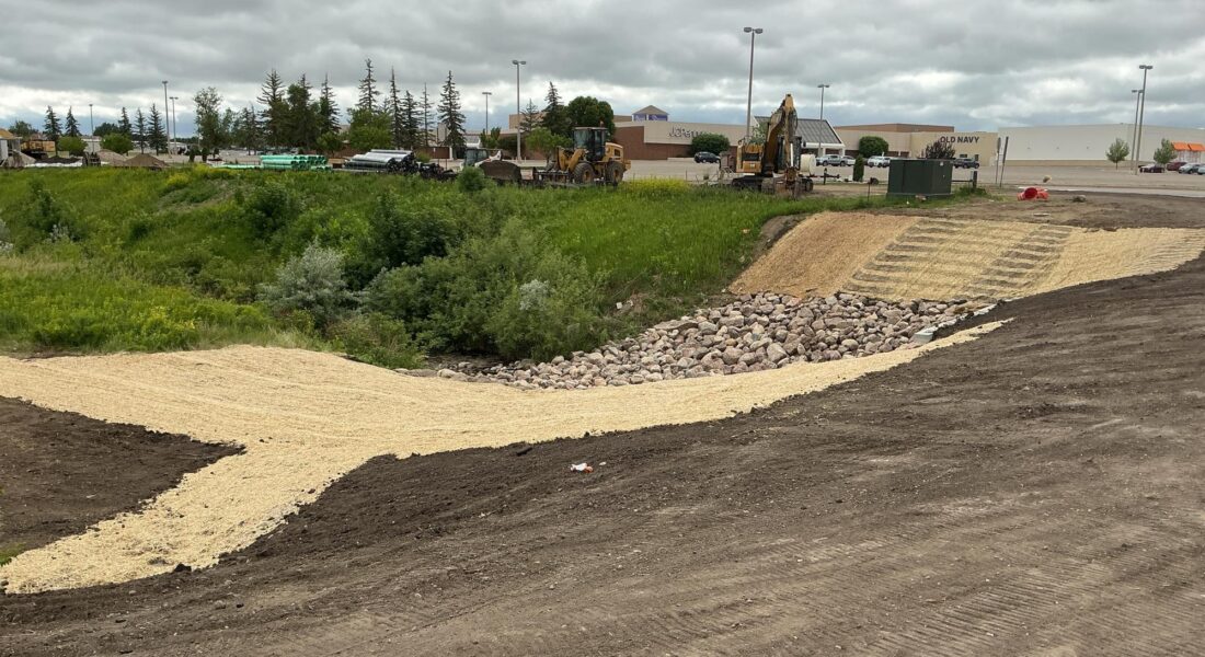 Construction site with machinery, rock slope, gravel paths, overcast sky.