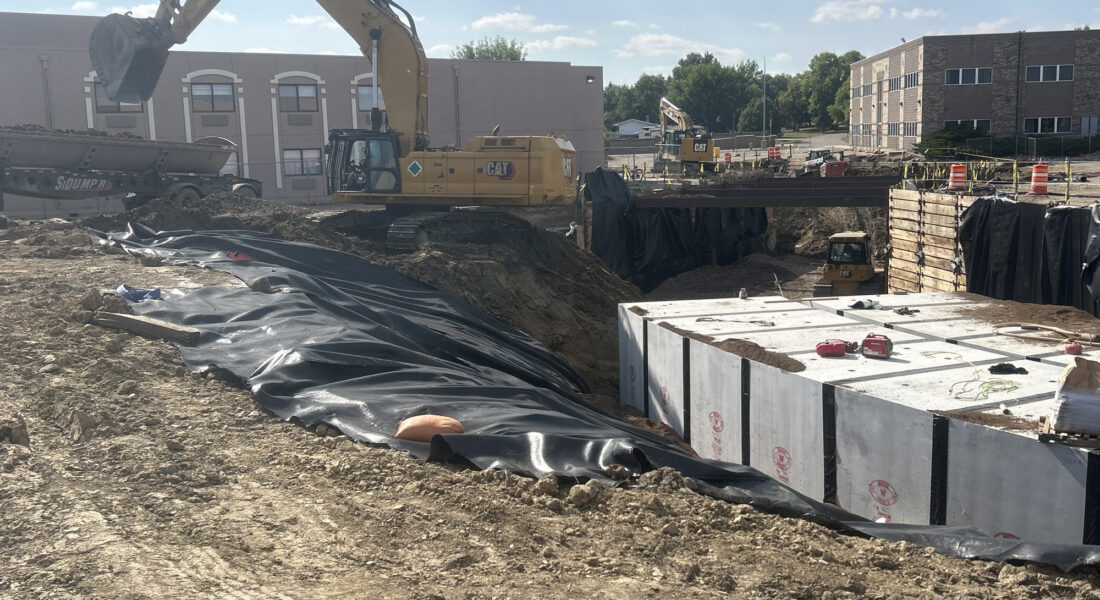Excavators dig among concrete, plastic sheets, and dirt piles.