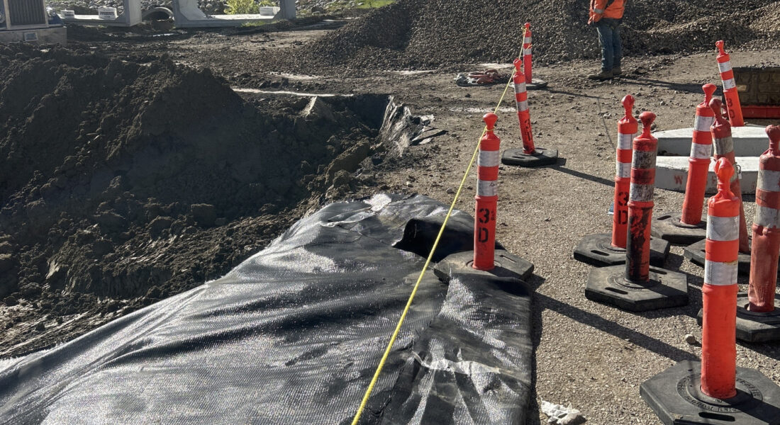 Construction site with materials, safety cones, worker, tape, trees.