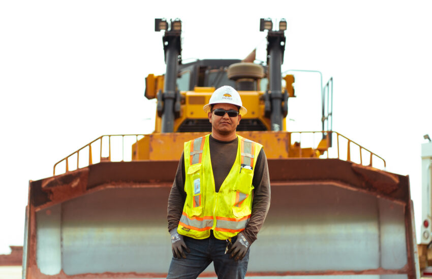 Worker in safety gear stands before a large bulldozer.