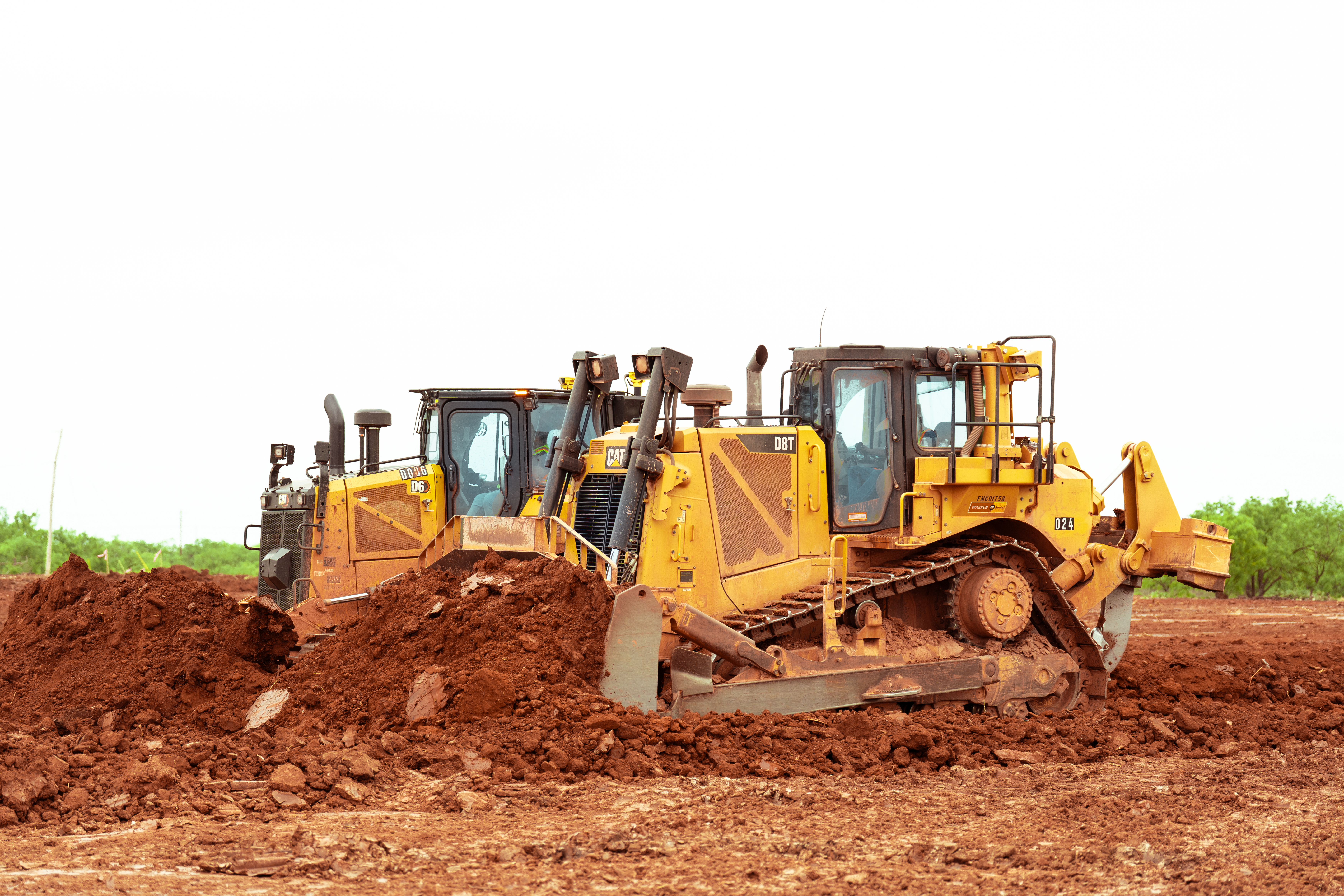 Two bulldozers pushing red dirt with a clear sky