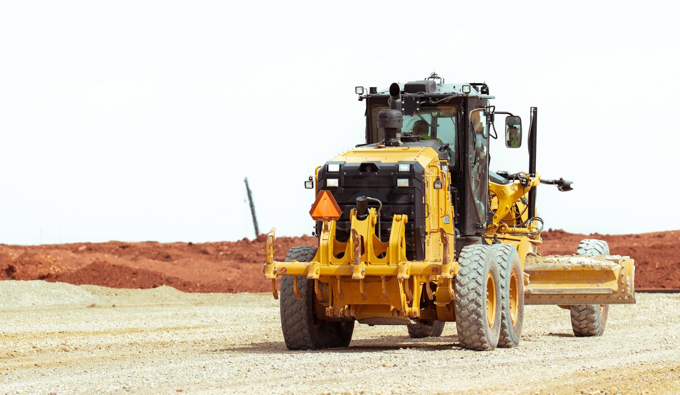 Yellow road grader parked on gravel at a construction site.