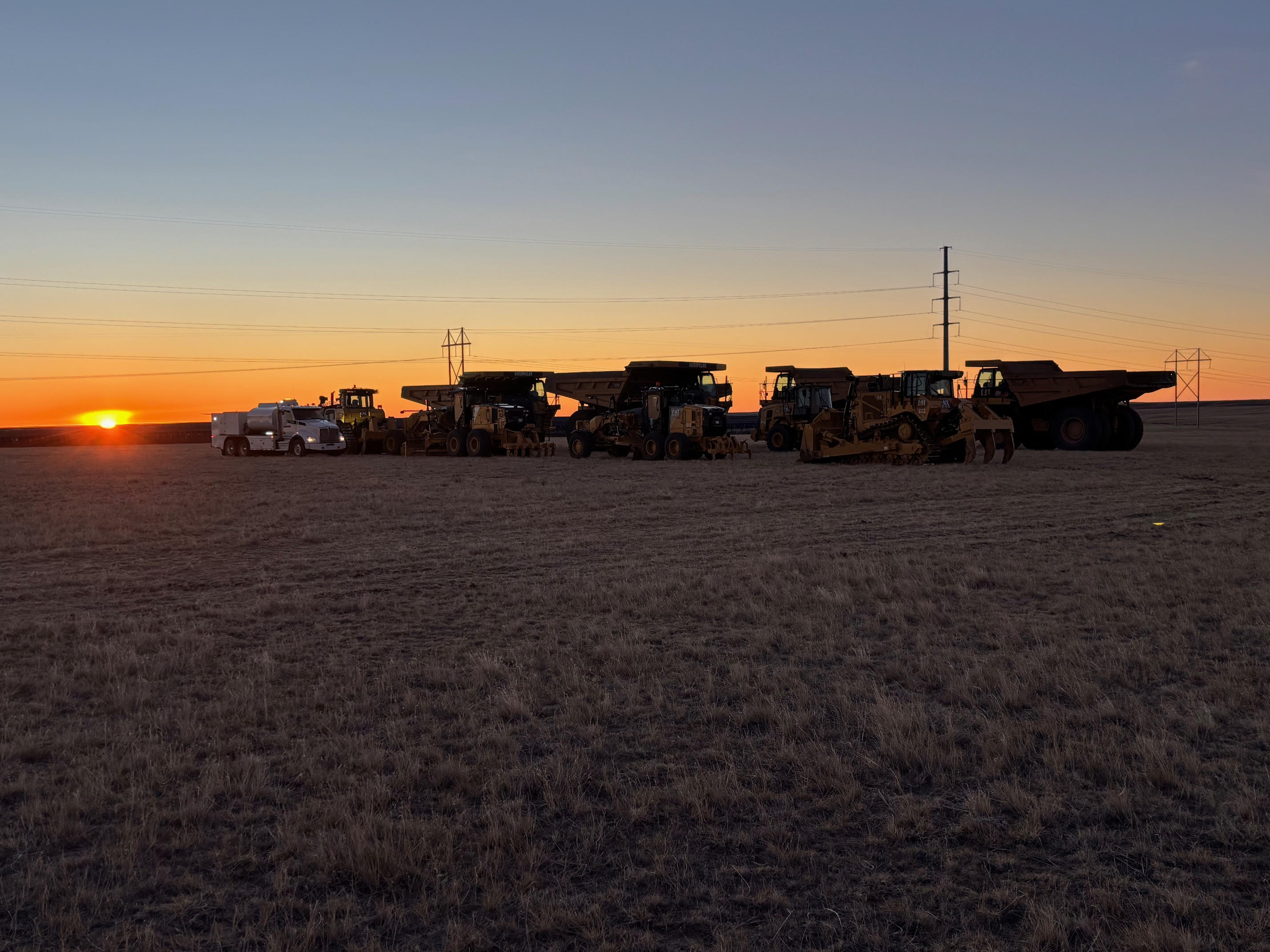 Construction vehicles lined up on a field at sunset.