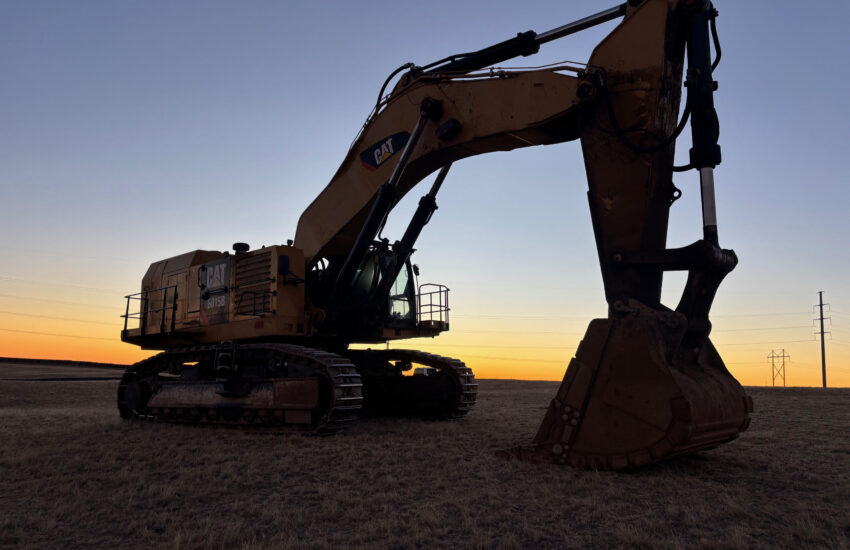 Caterpillar excavator silhouetted at sunset on grassy field.