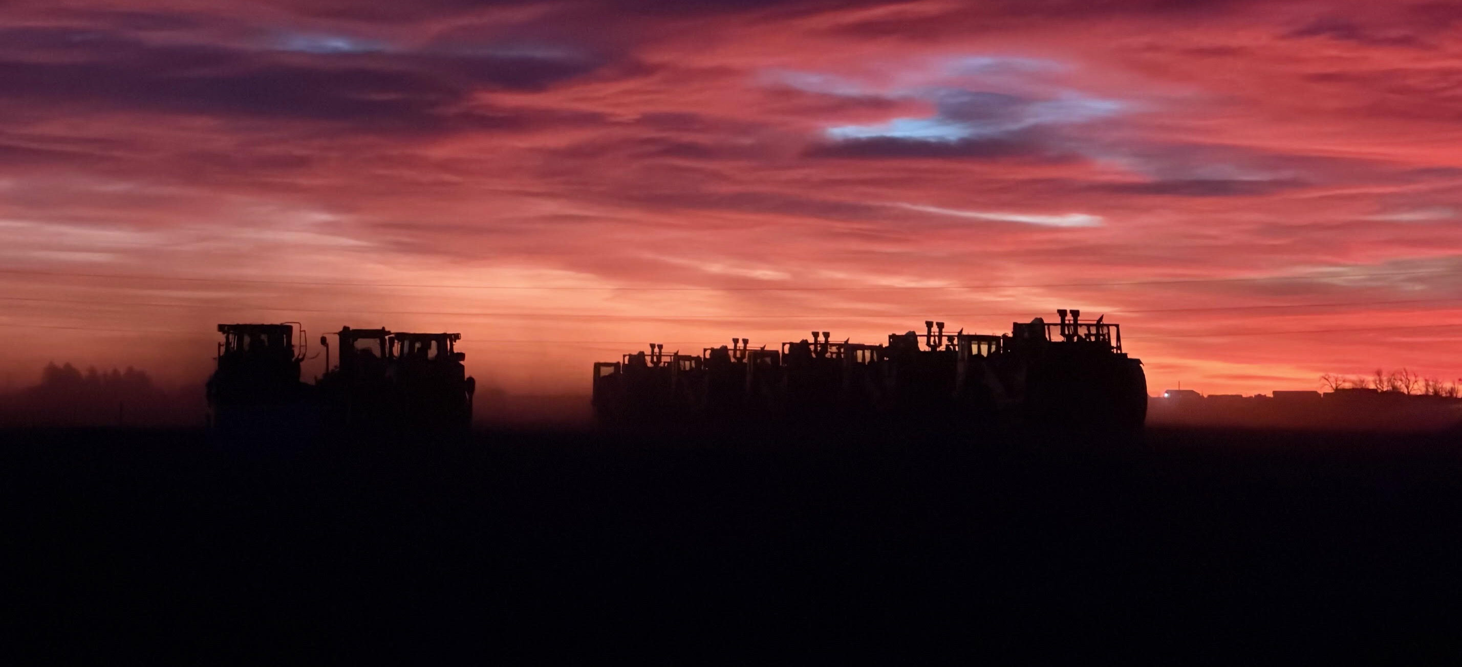 Construction vehicle silhouettes in a field at sunset.